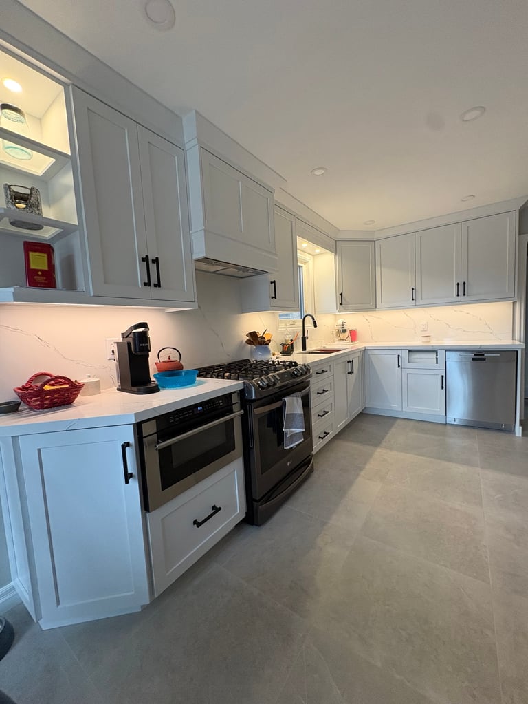 Modern white kitchen with stainless steel double ovens, white cabinetry, white countertops, and concrete flooring