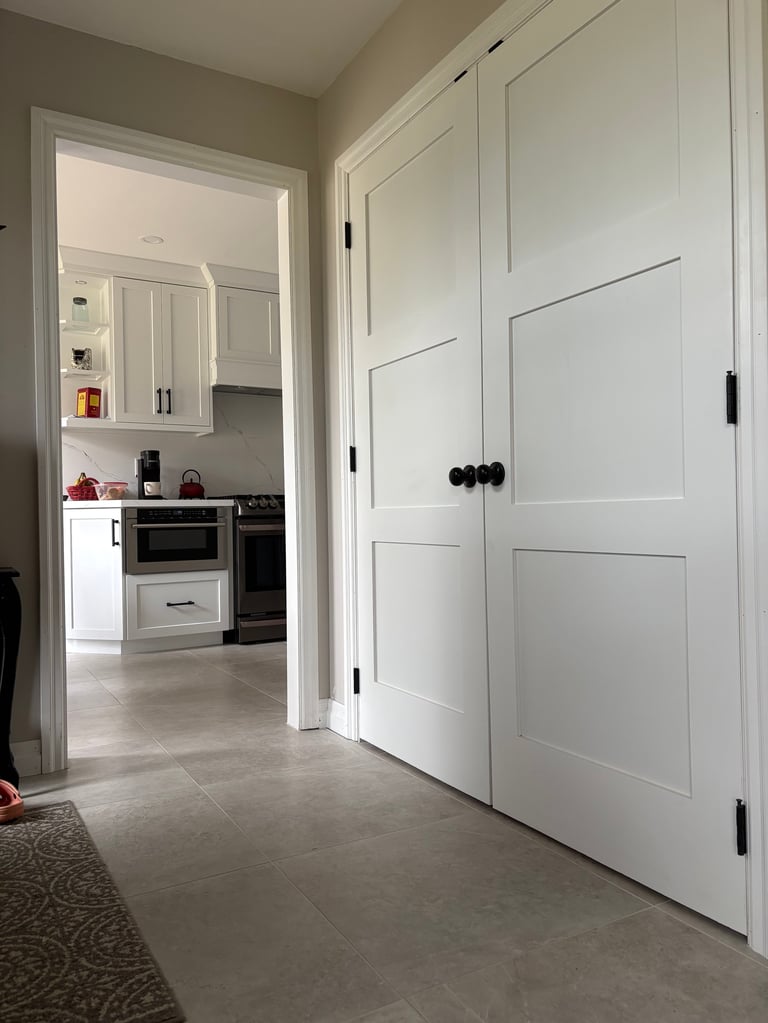 Modern entryway with white panel closet doors and open doorway revealing contemporary kitchen with white cabinets and stainless steel appliances