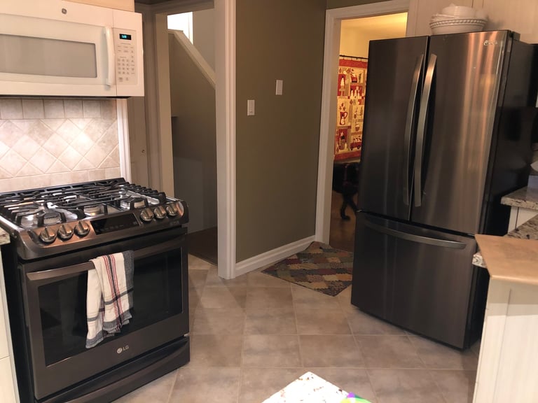 Modern kitchen with black gas stove, stainless steel refrigerator, and white microwave on beige tile floor