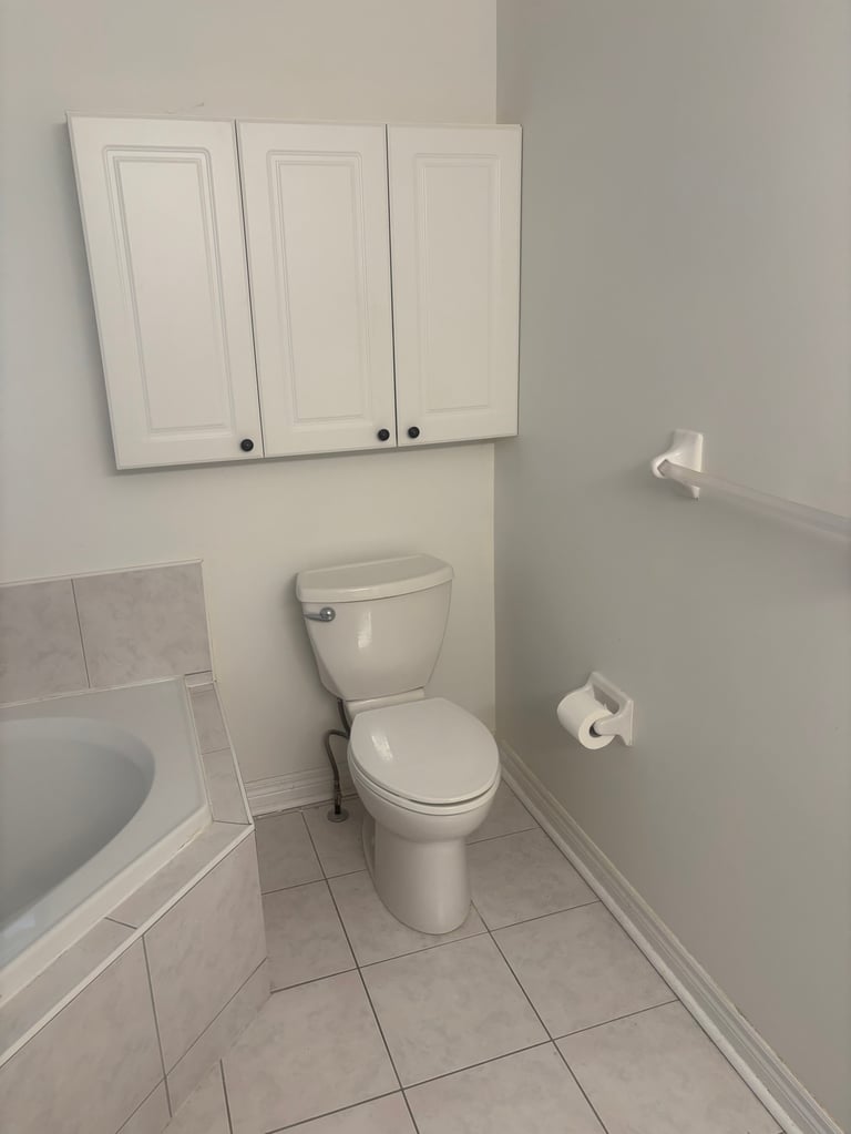 Clean bathroom interior with white toilet, tile flooring, cabinets, and toilet paper roll holder on wall