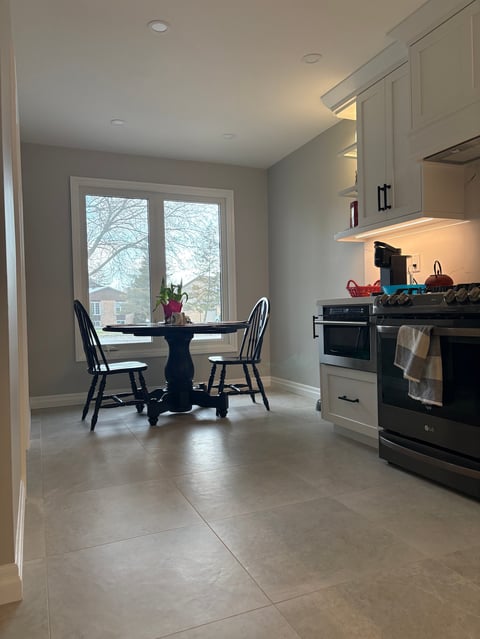 Modern kitchen with dining area, large windows, black dining table with chairs, white cabinetry, and stainless steel appliances