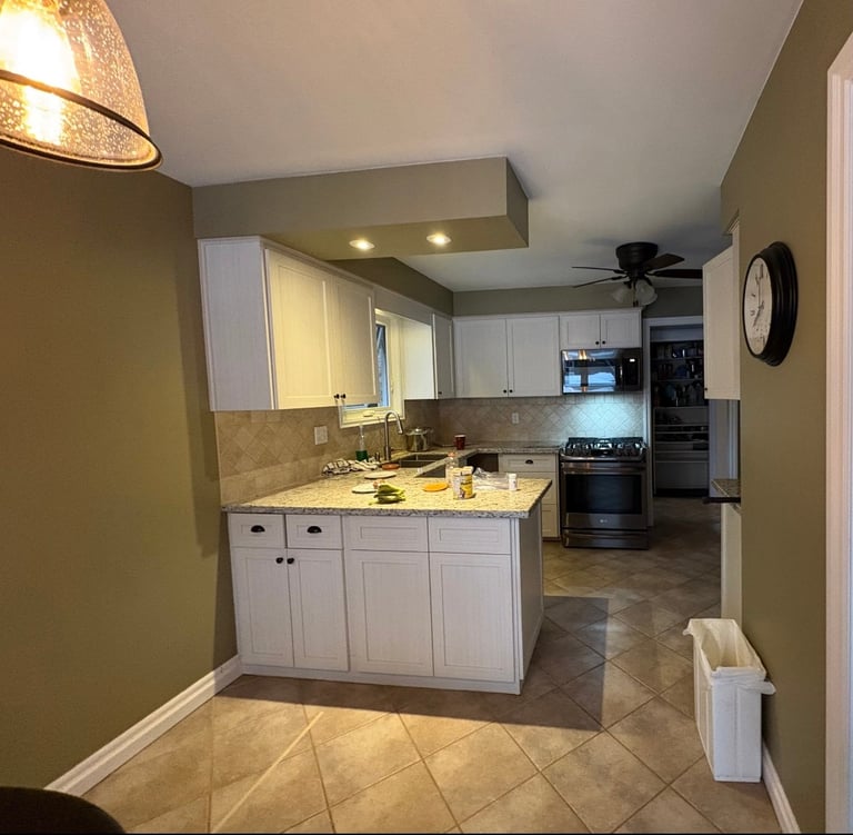 Modern kitchen with white cabinetry, granite countertops, stainless steel appliances, and olive green walls with tile flooring