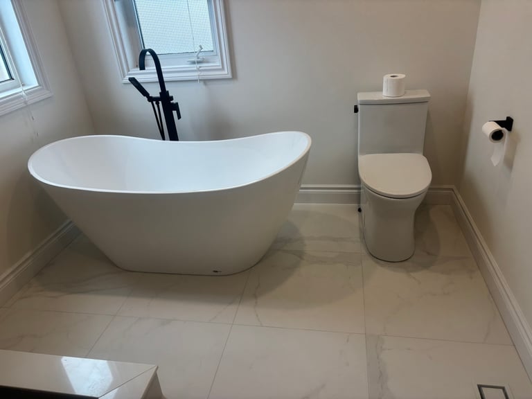 Modern bathroom with white freestanding soaking tub, toilet, and beige tile flooring
