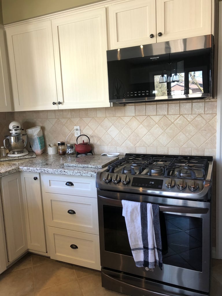 Modern kitchen with white cabinetry, granite countertops, black stainless steel gas range, and diagonal subway tile backsplash