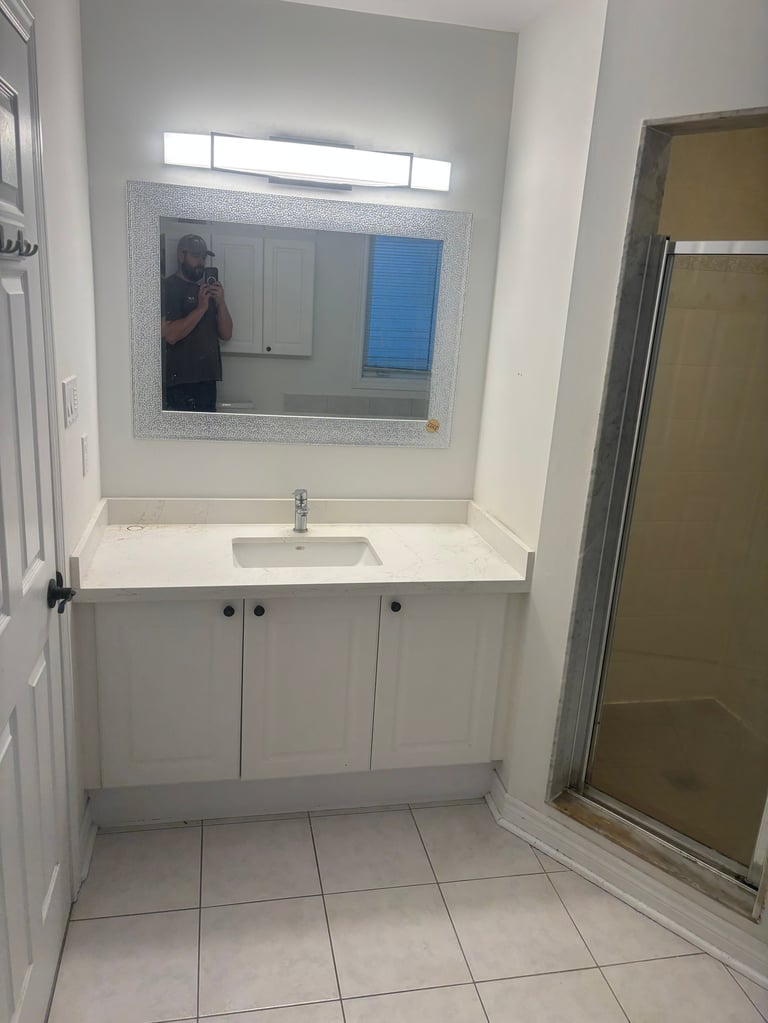 Modern bathroom with white vanity, single sink, large mirror with frame, tile floor, and glass shower enclosure