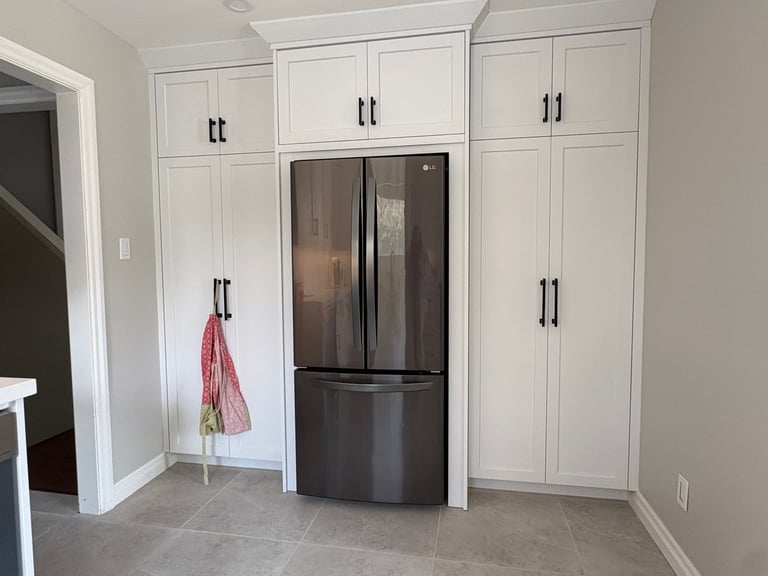 Modern kitchen with white cabinetry surrounding a black French-door refrigerator, featuring tile flooring and a red tote bag hanging on a door handle