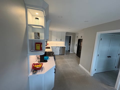 Modern kitchen and entryway with white cabinetry, built-in shelving, dual sinks, and light gray flooring