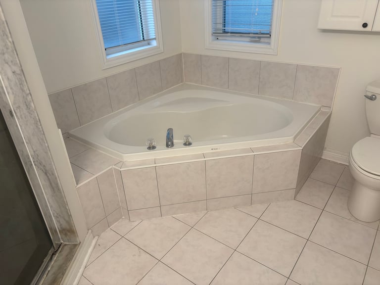 Modern white bathroom with corner soaking tub, tile walls and floor, toilet, and windows with blue blinds
